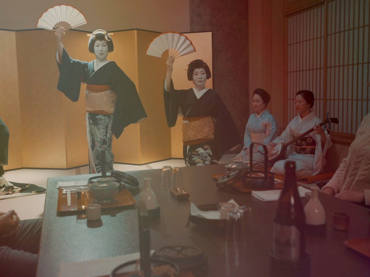Geisha dancing with fans before guests at a private ozashiki